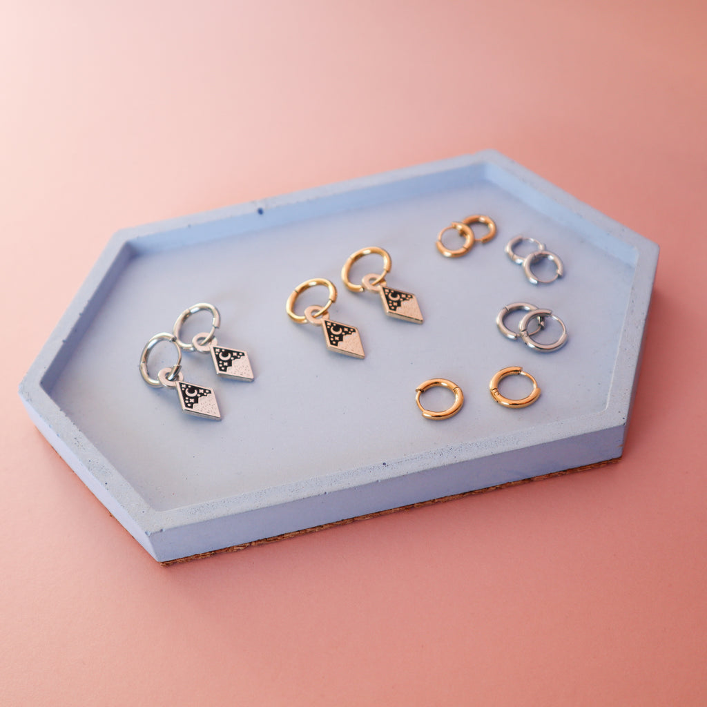 A selection of mountain earrings and huggie hoops on a blue concrete tray.