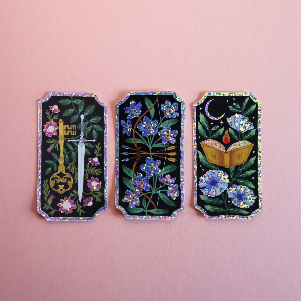 Three rectangular glitter stickers with dagger, bow and arrow, and a book motif.