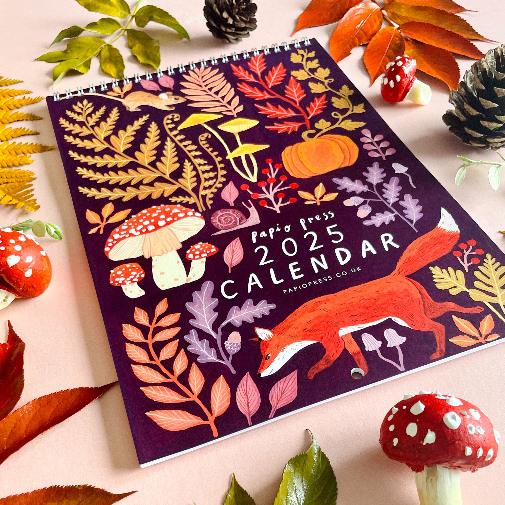 The 2025 Papio Press Florals & Animals Calendar features a vibrant cover with autumn leaves, mushrooms, a pumpkin, and a fox, beautifully illustrated by Papio Press.