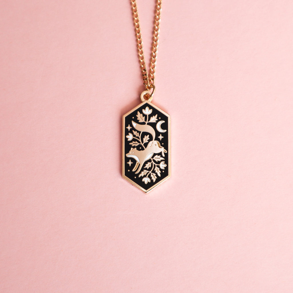 A gold floral fox necklace on a pink background.