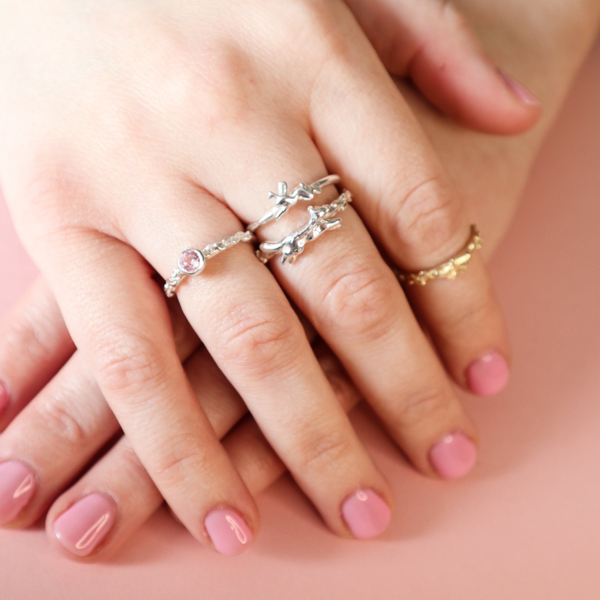A hand wearing several Papio Press rings. Featuring the Pink Sapphire, Jackalope, Fox and Butterfly designs.