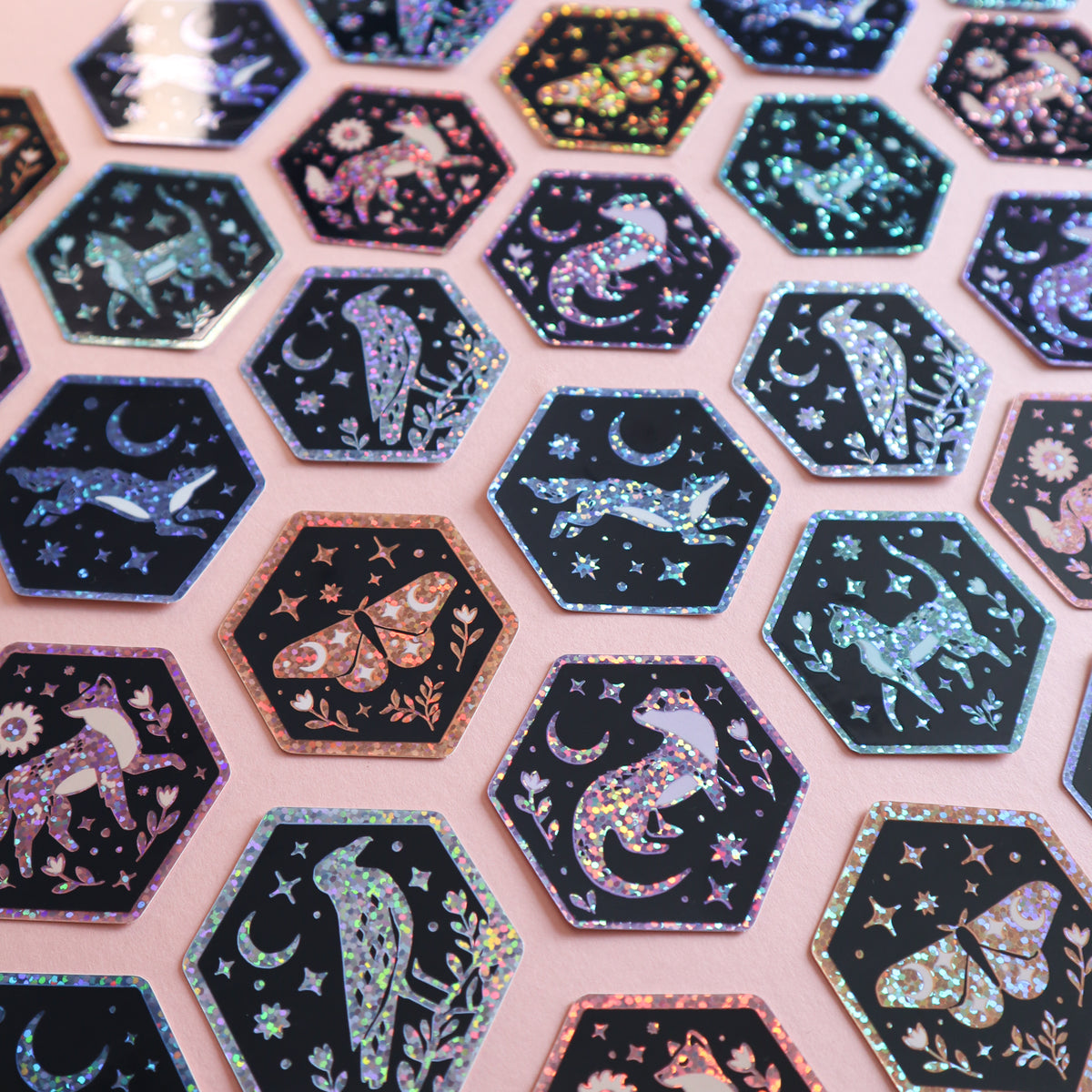 Hexagonal stickers featuring glittery celestial and animal designs on a pink background.