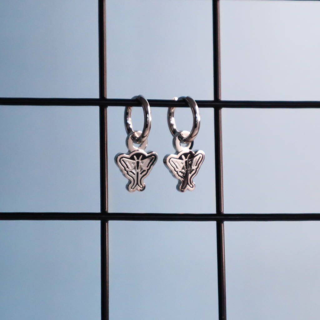 A pair of silver moth earrings hanging from a black wire on a blue background.