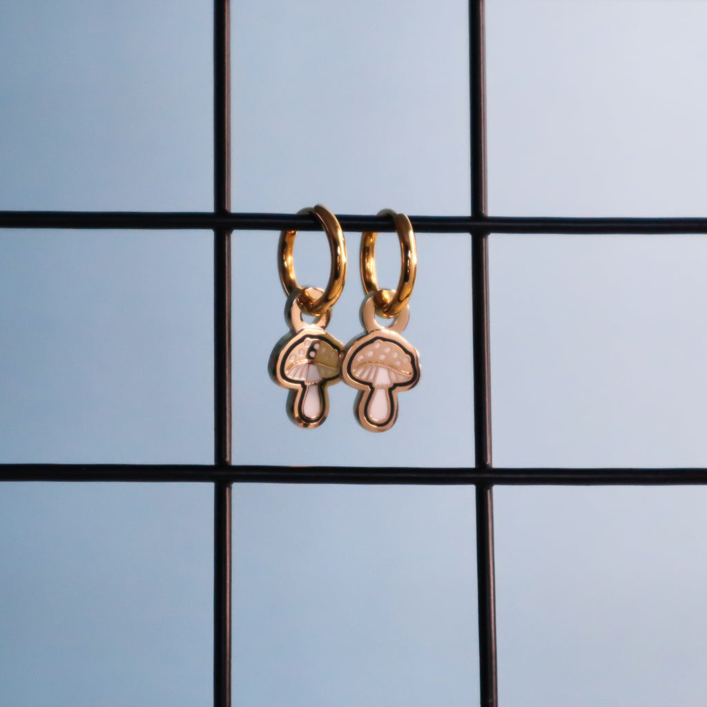A pair of gold mushroom earrings hanging from a black wire on a blue background.