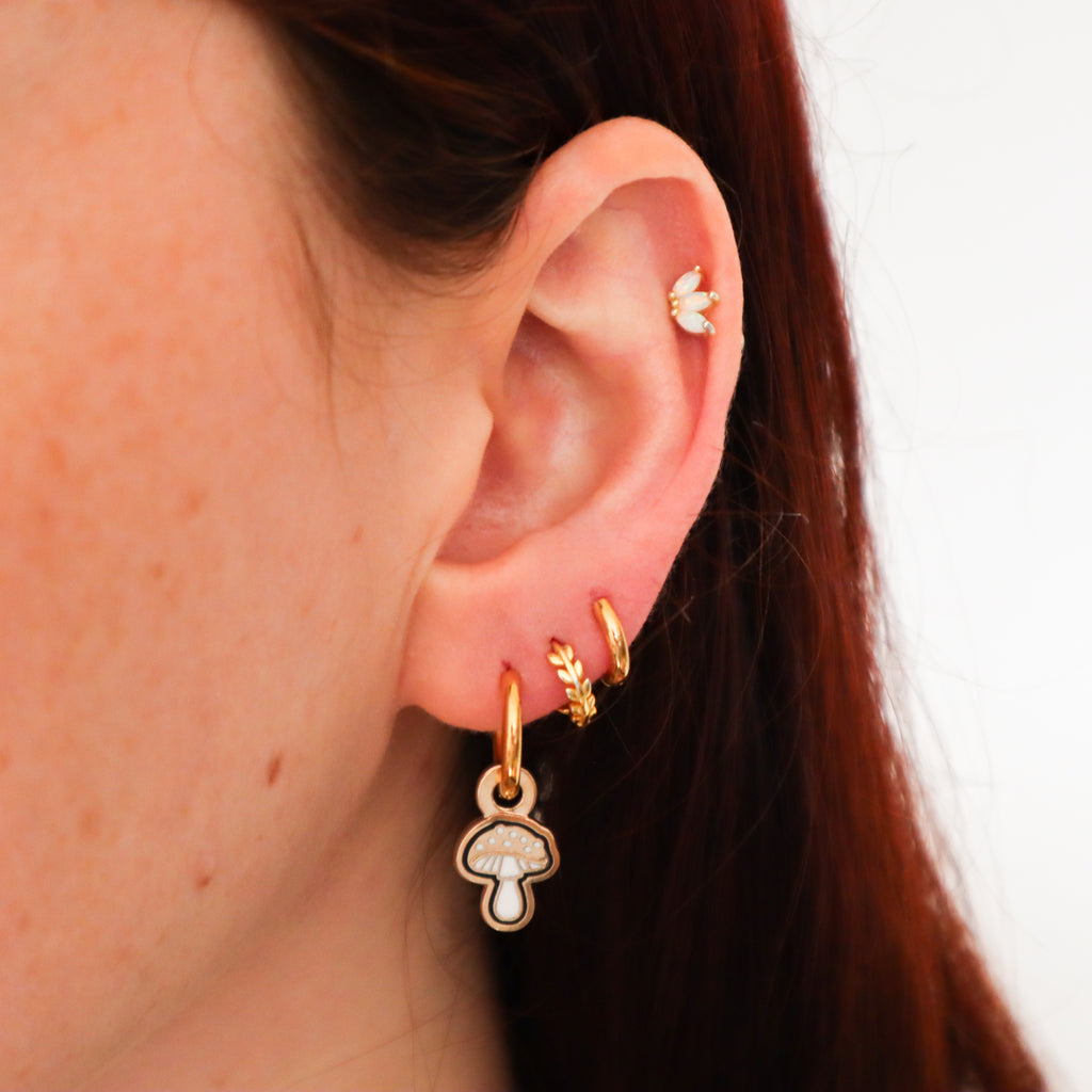 A woman's ear featuring several different earrings including a gold mushroom earring.