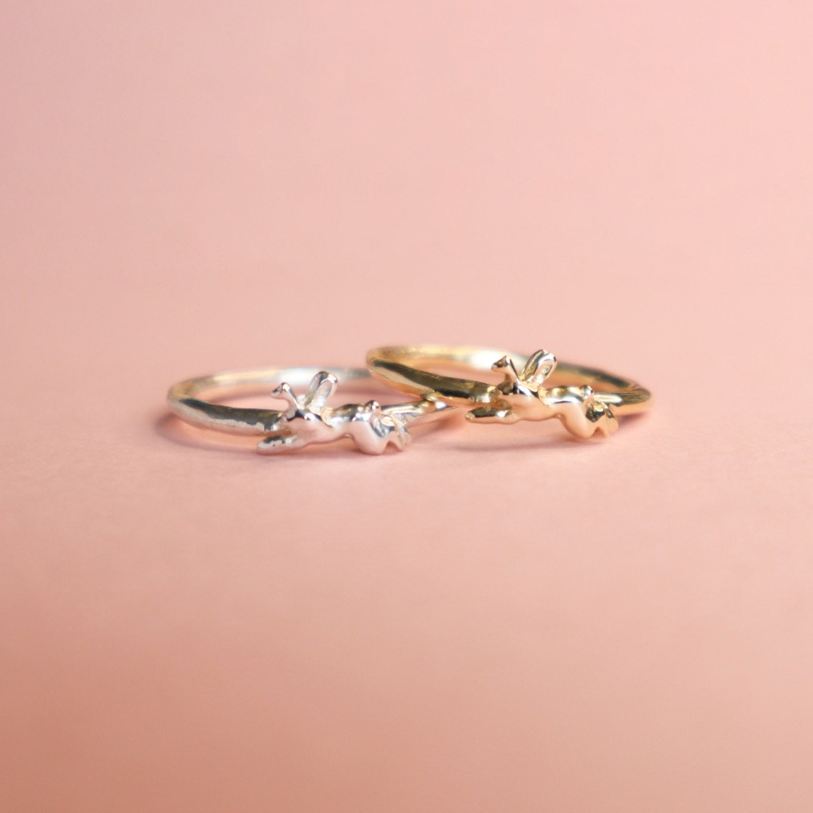 Two Jackalope rings, one gold and one silver on a pink background