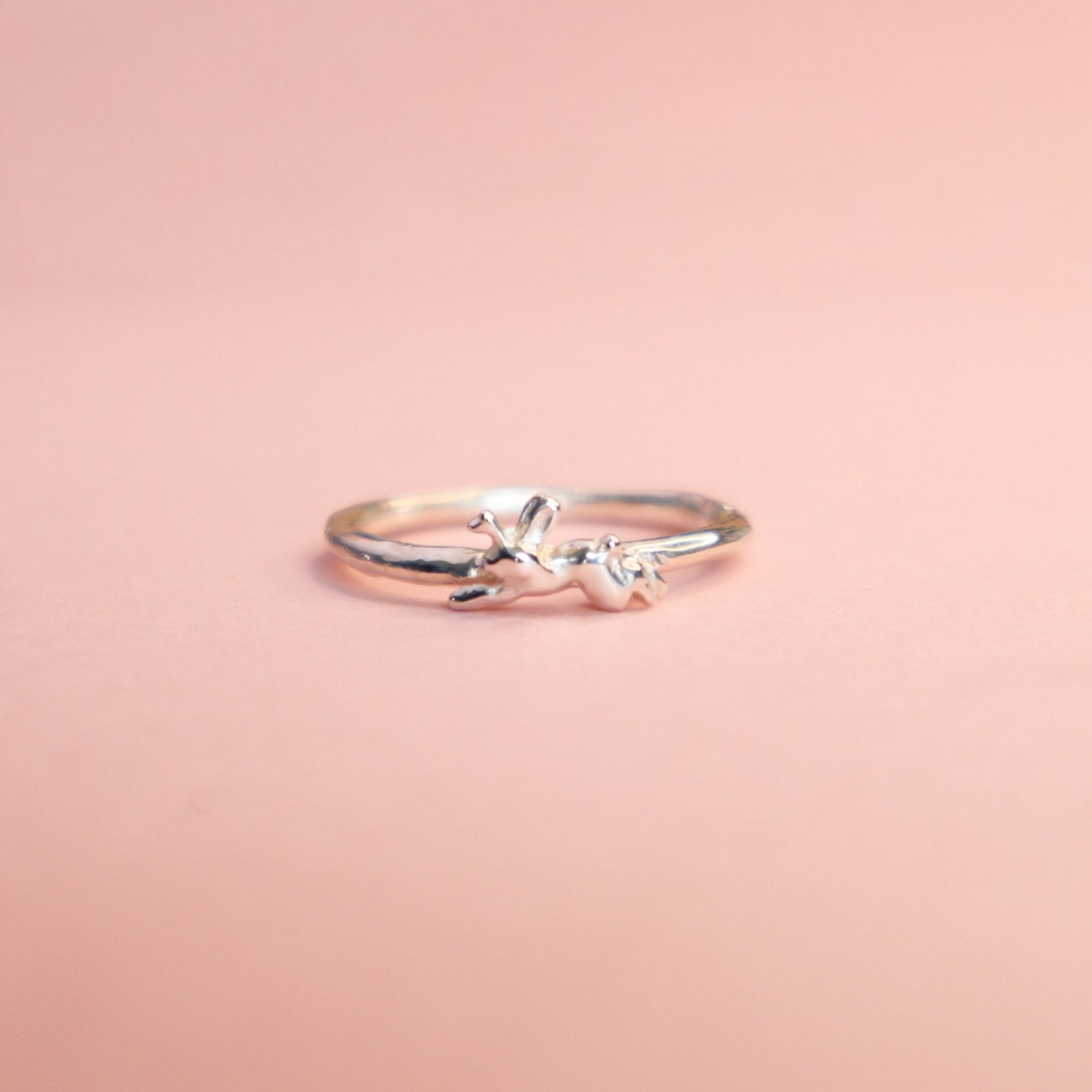 Silver ring with a small jackalope design on a pink background