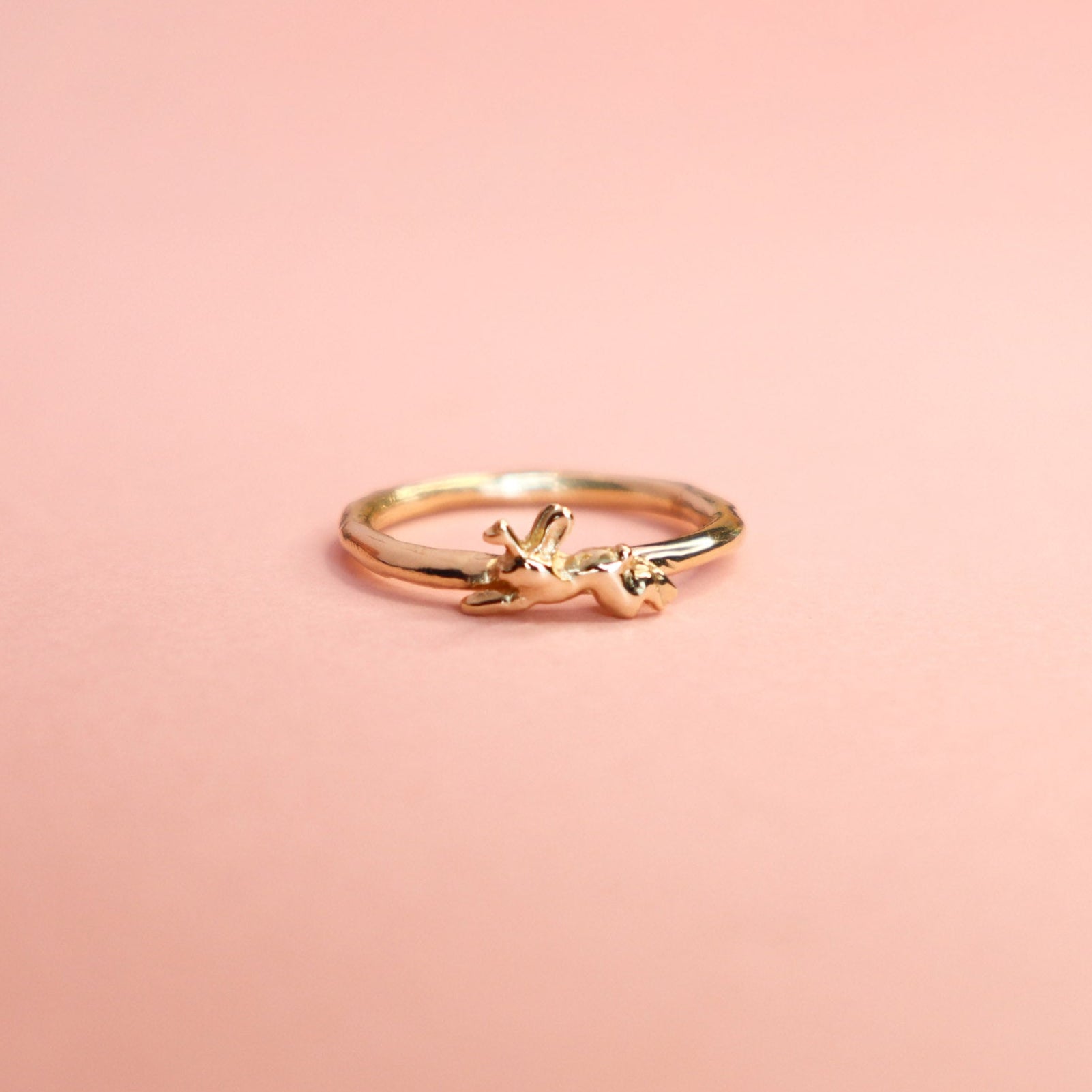 Gold ring with a small jackalope design on a pink background