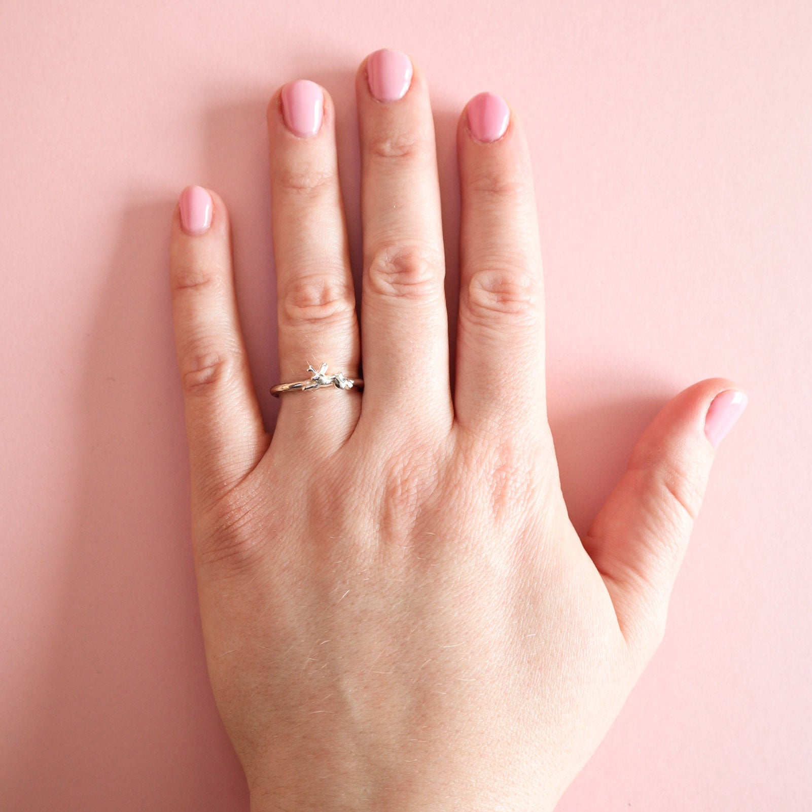 Hand with a silver jackalope ring on a pink background