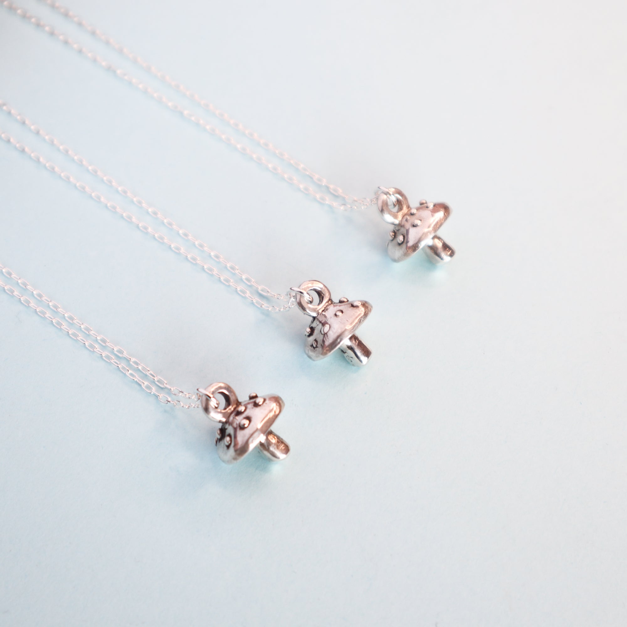 Three silver mushroom pendants on a light blue background.