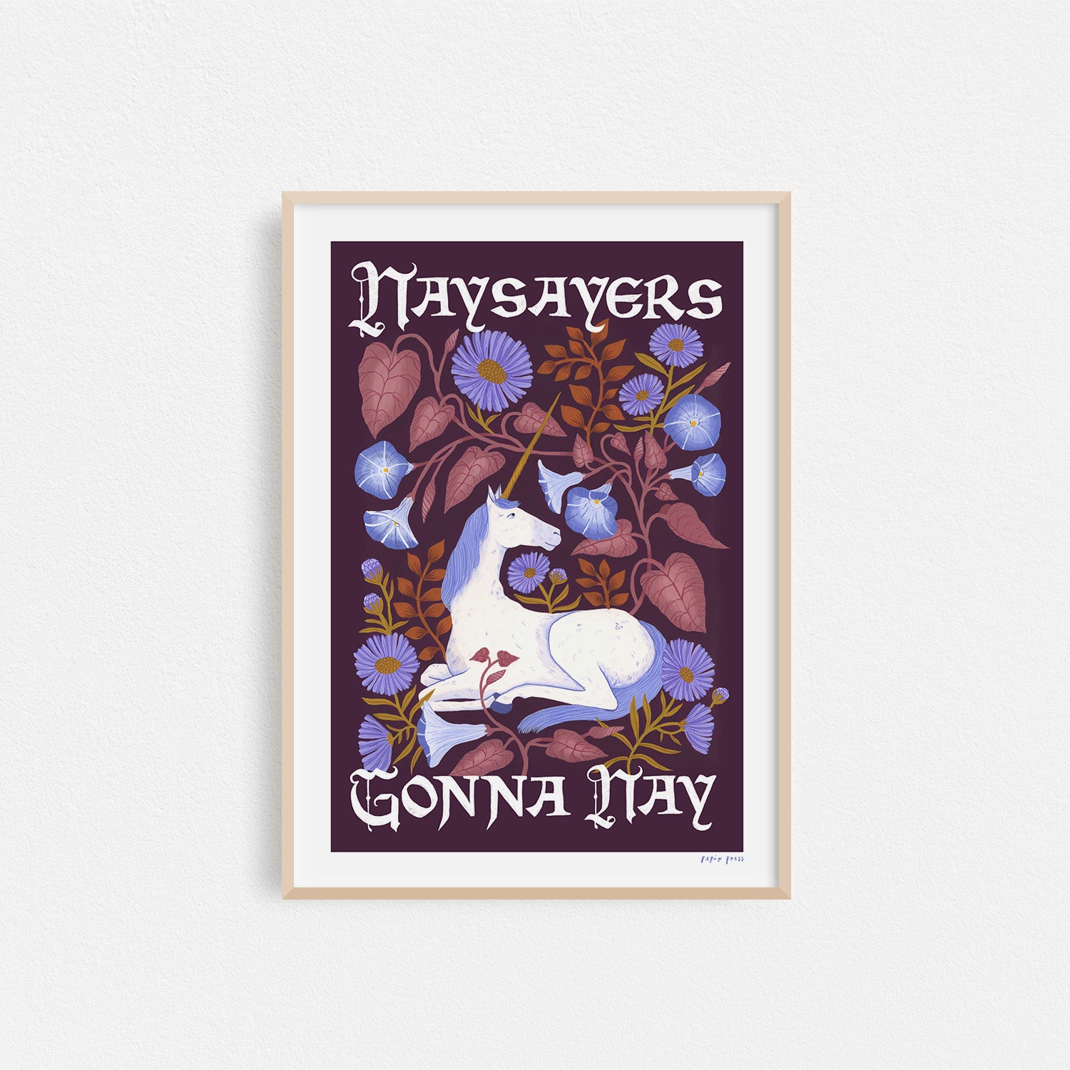 A photograph of a framed unicorn print. The unicorn is surrounded by flowers. It features the type 'Naysayers gonna nay' in a script font. 