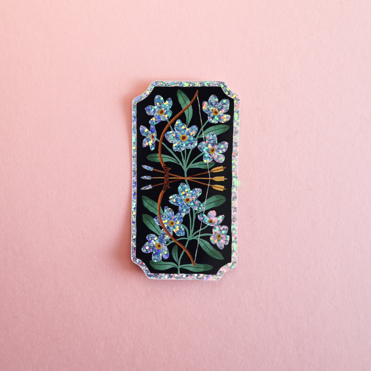 A rectangular sticker with a black background, decorated with blue forget-me-not flowers, green leaves, and a brown bow and arrow, finished with a holographic glitter border, set against a solid pink background.