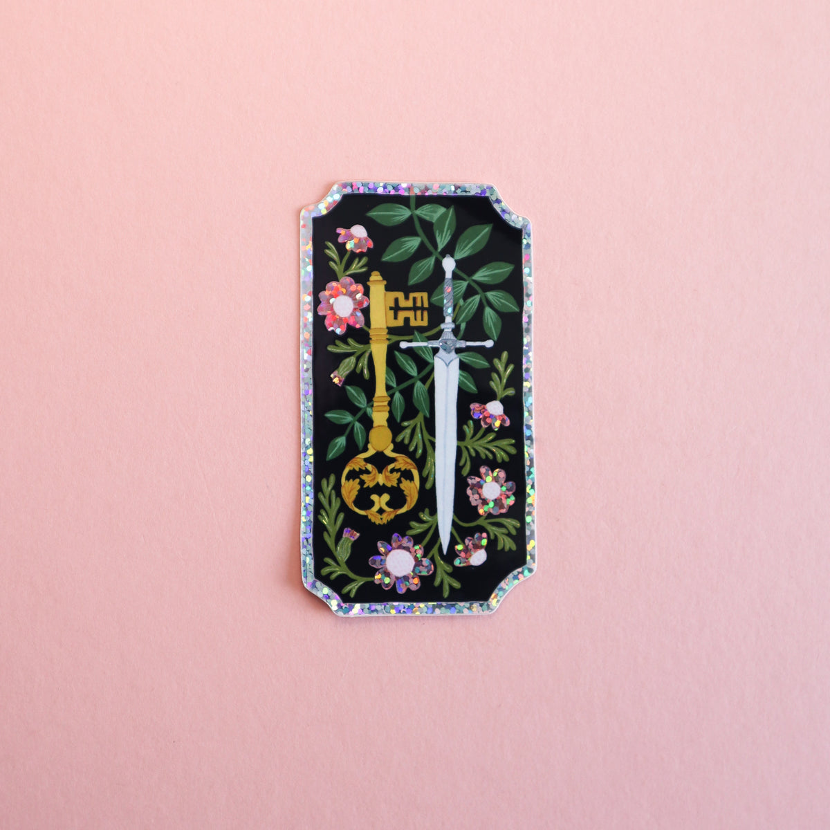 A rectangular sticker with a black background, featuring a gold key, a silver sword, and pink flowers with green leaves, bordered by a glittery blue and pink frame, set against a solid pink background.