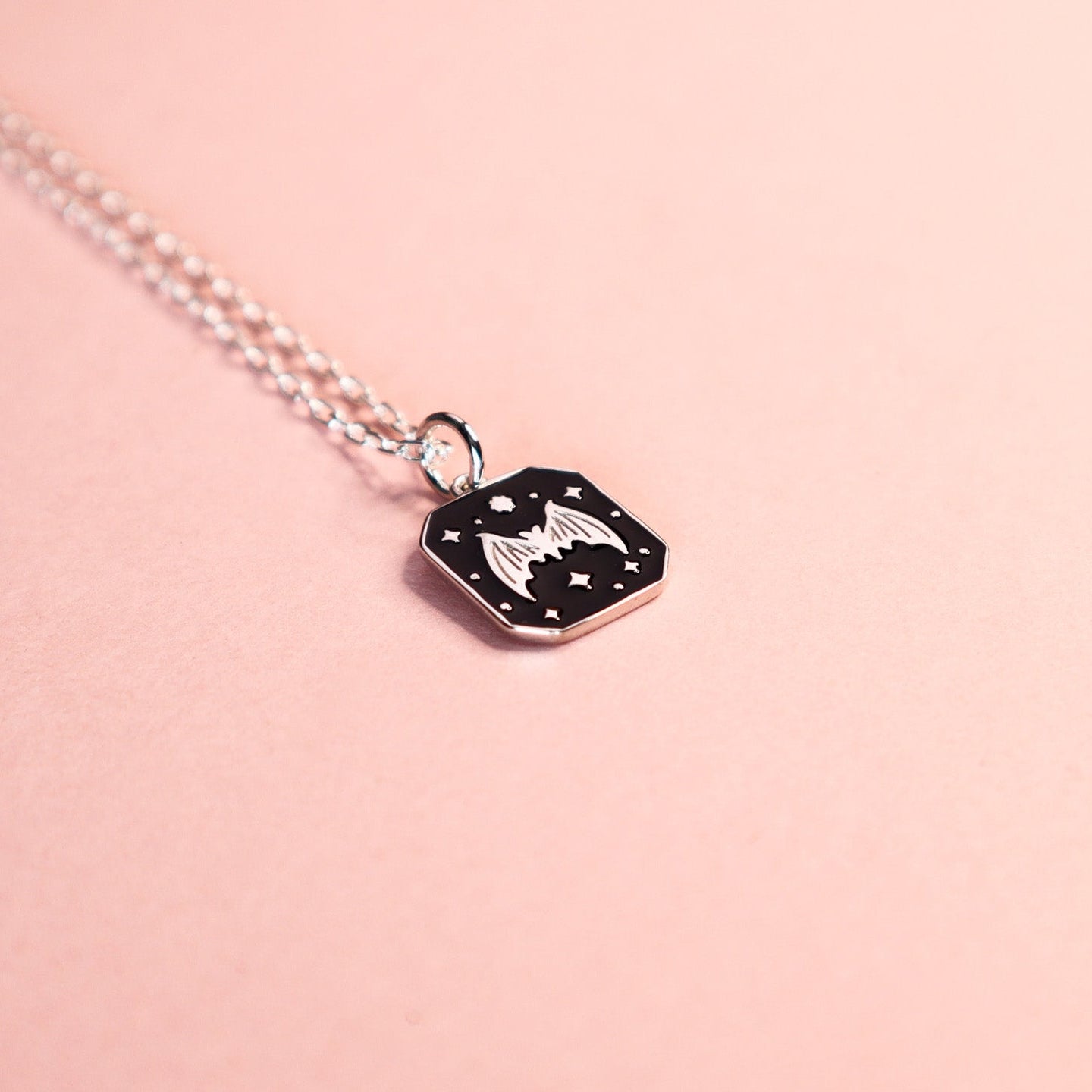 Square silver pendant featuring a Bat and stars with black enamel details. Taken on a light pink background.