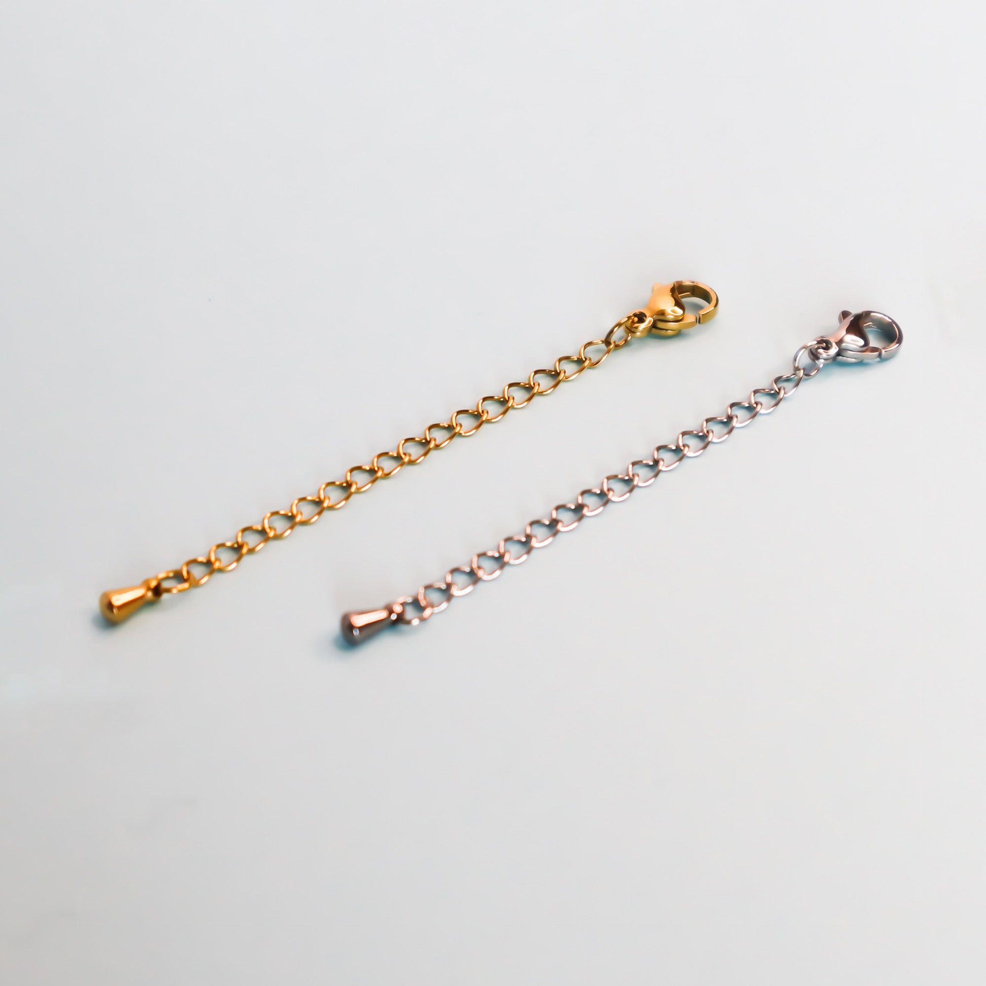 Two necklace extenders, one gold and one silver on a light blue background.