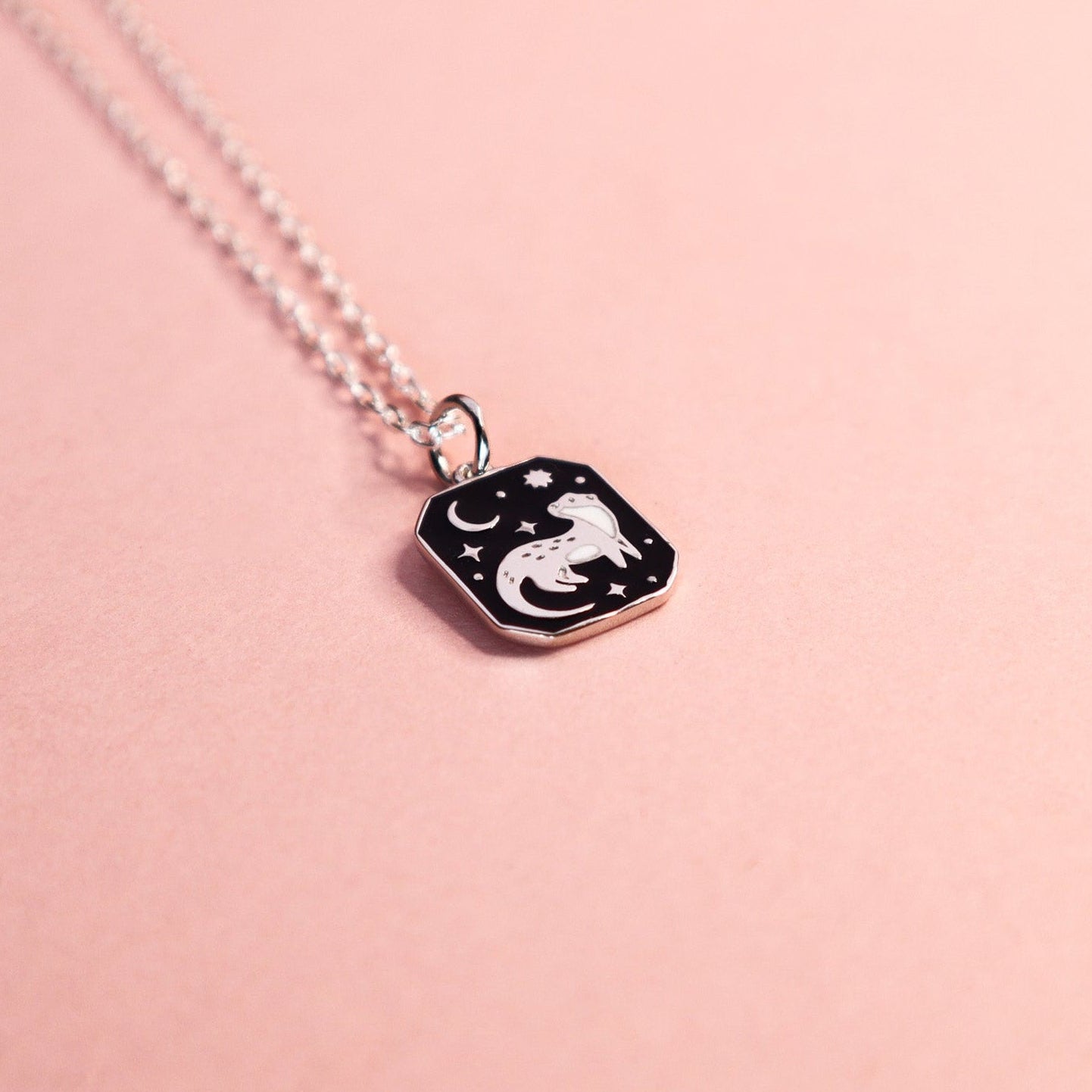 Necklace with a square pendant featuring an otter design on a pink background.