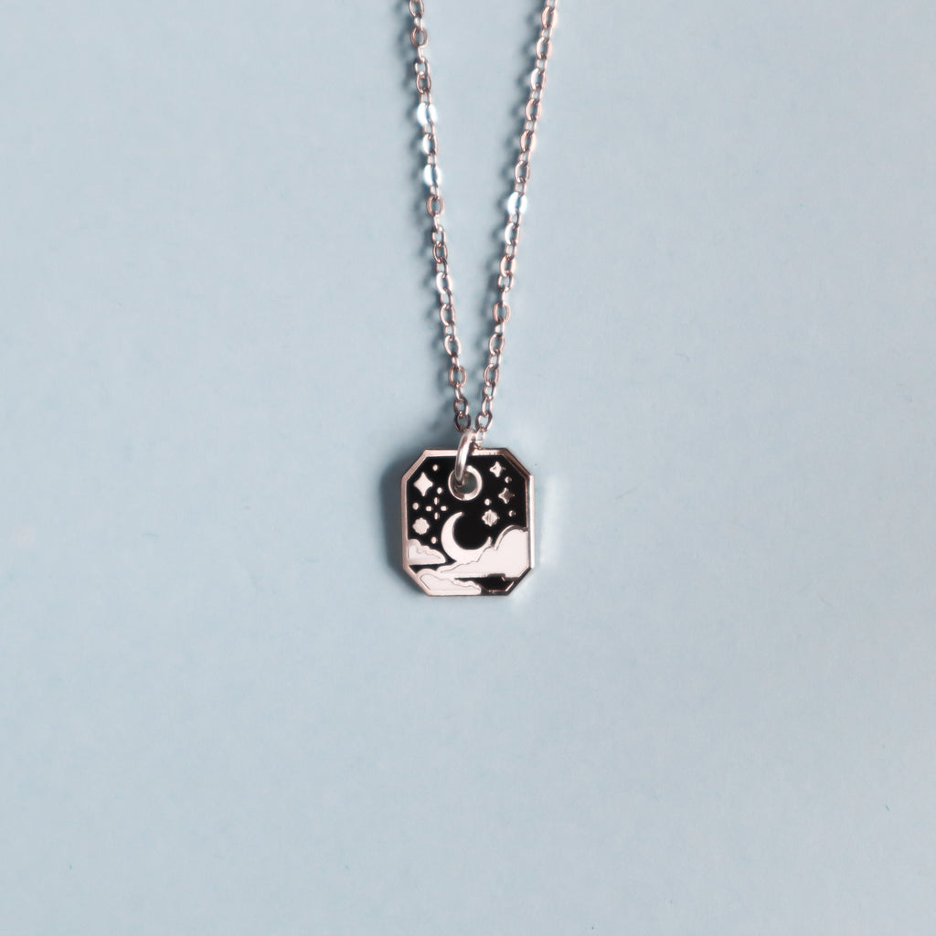 A silver starry sky necklace on a light blue background.