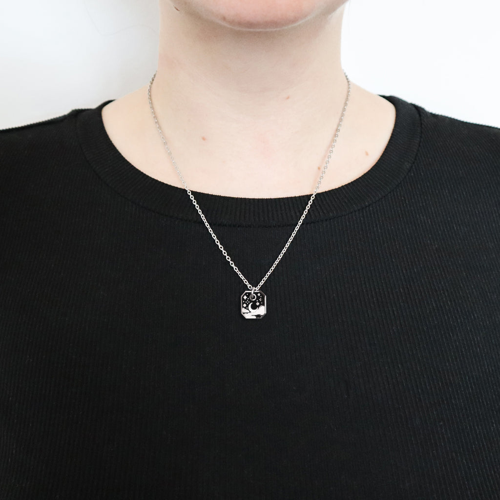 A silver starry sky necklace being worn by a woman in a black top.