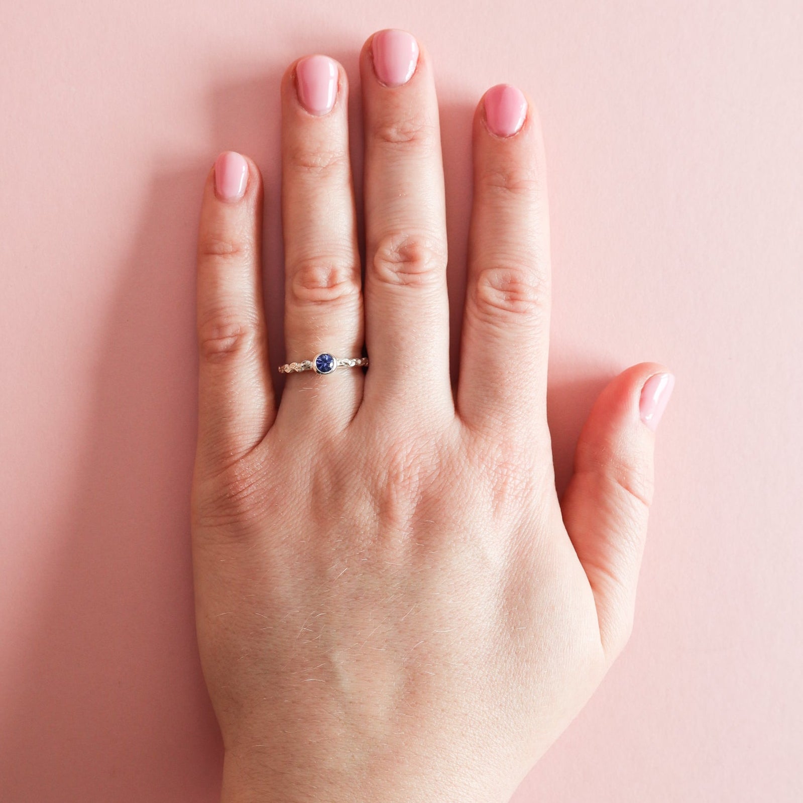 A hand wearing a silver ring featuring a blue sapphire. 