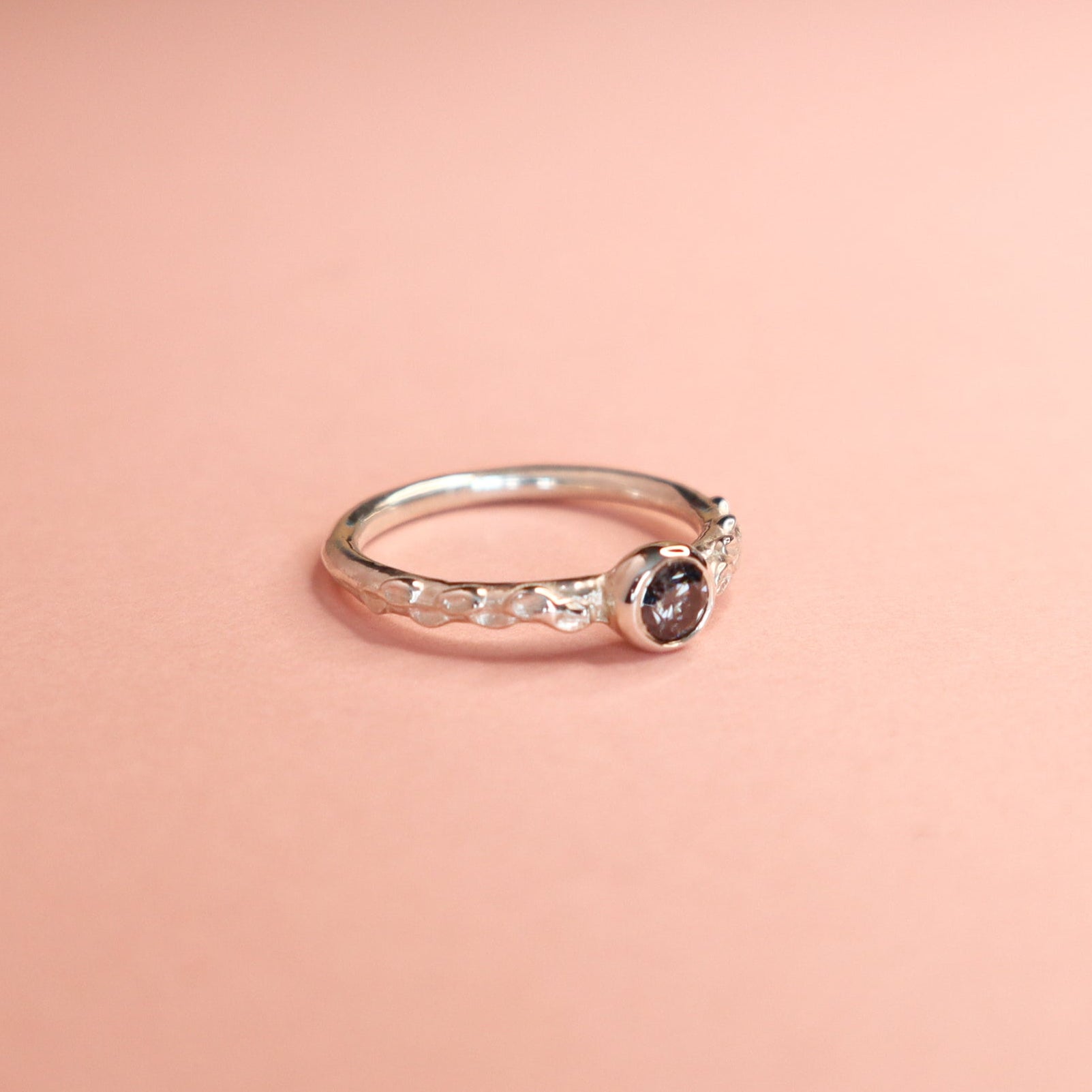Silver ring with a grey moissanite on a pink background