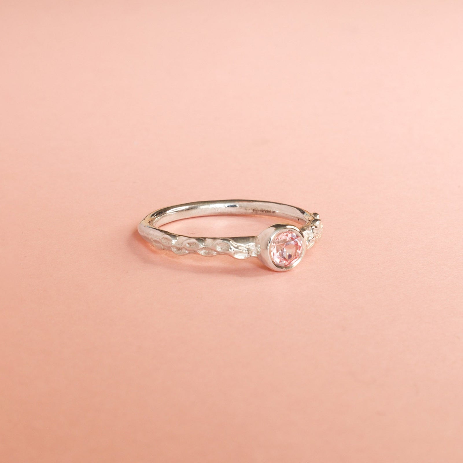 Silver ring with a pink sapphire on a pink background