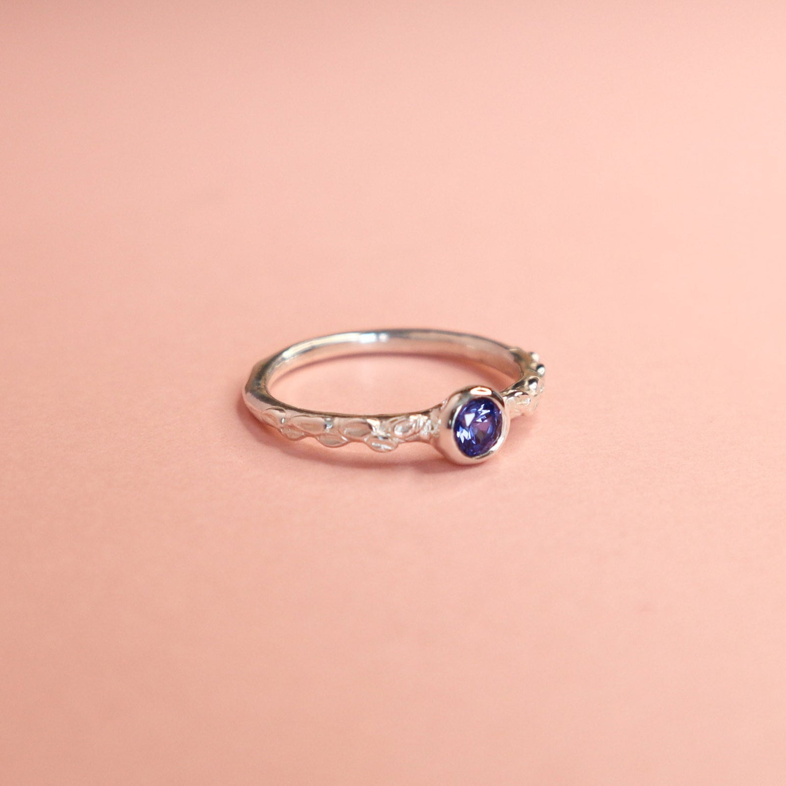 Silver ring with a cornflower blue sapphire gemstone on a pink background