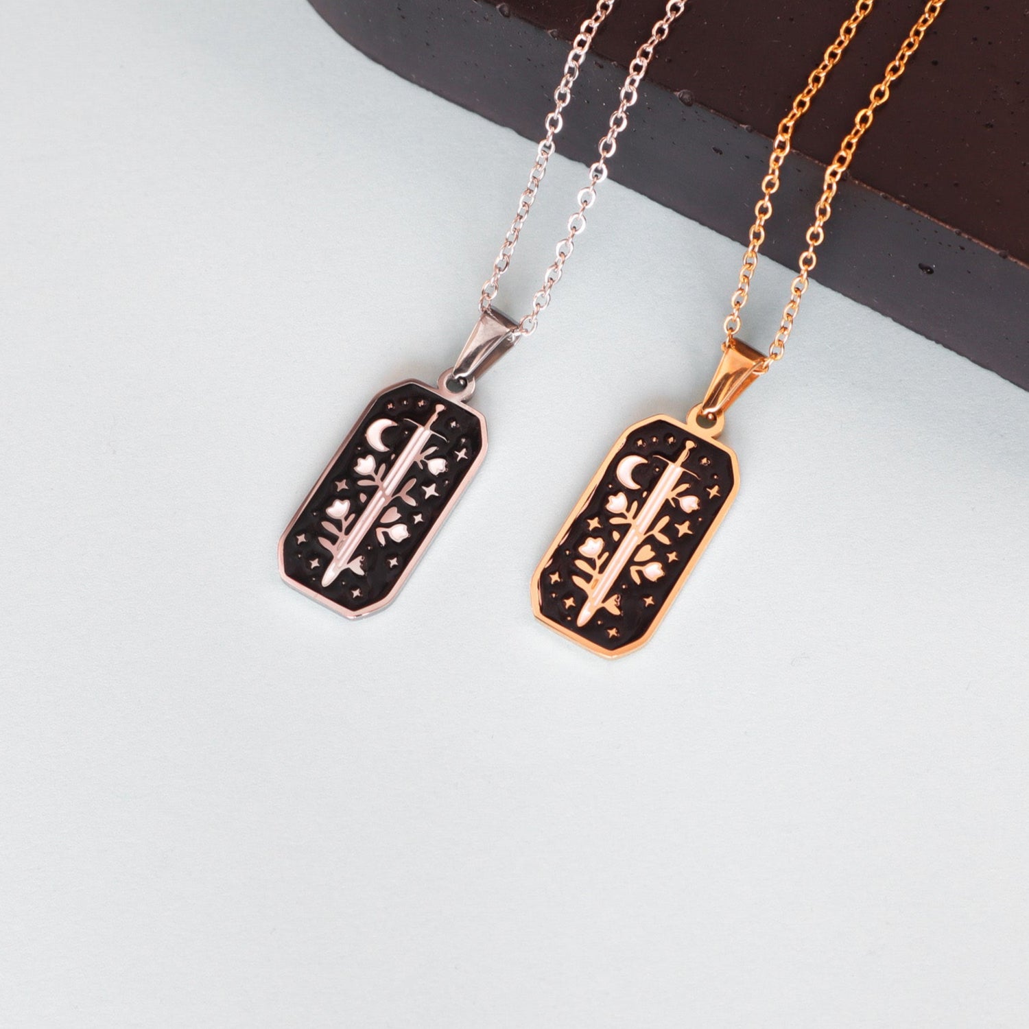 The Warrior Enamel Necklace by Papio Press features a rectangular pendant -available in stainless steel  or 18K gold-plate - with a celestial crescent moon and stars on enamel, bringing fantasy charm to any collection.