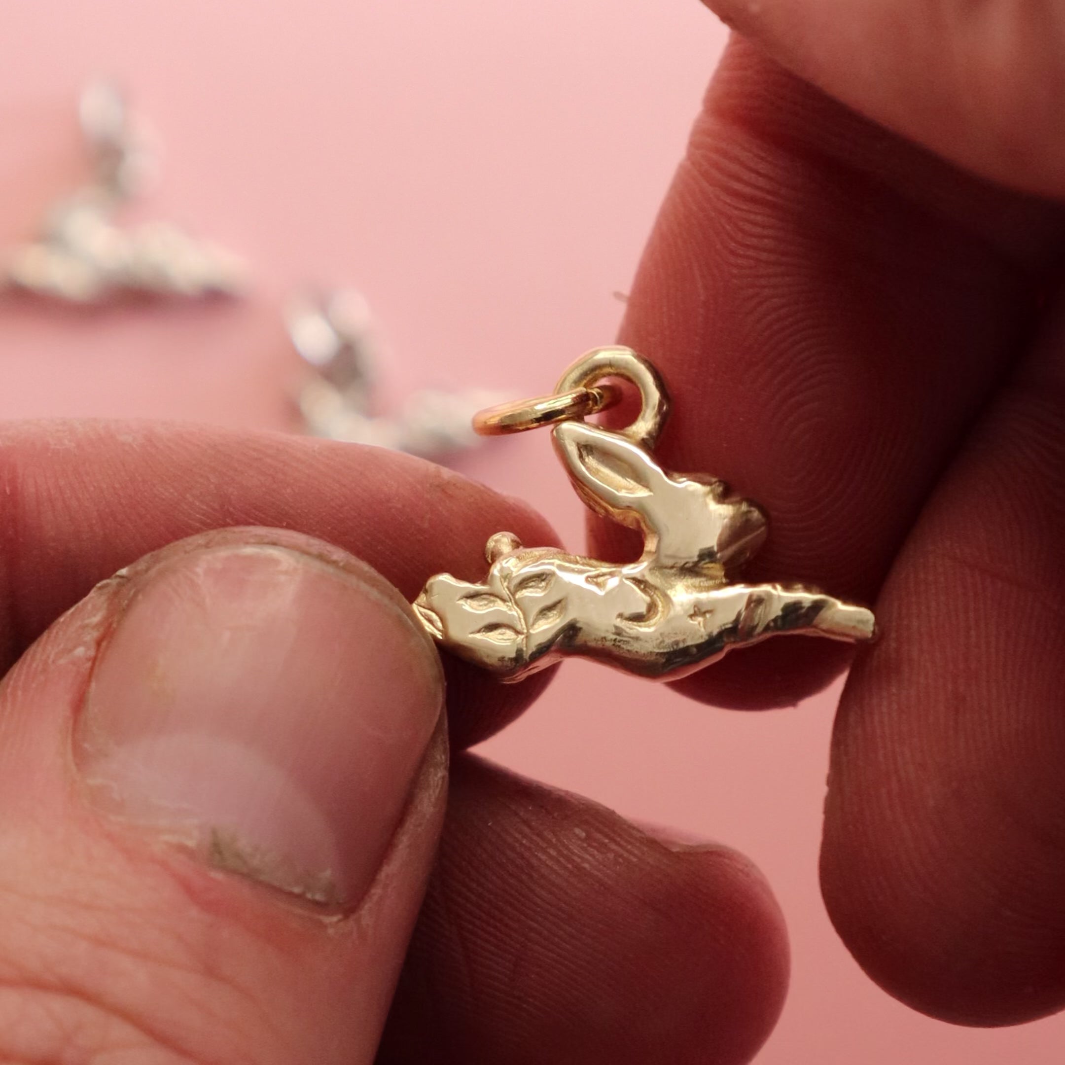 A hang holding a gold jackalope pendant charm. 