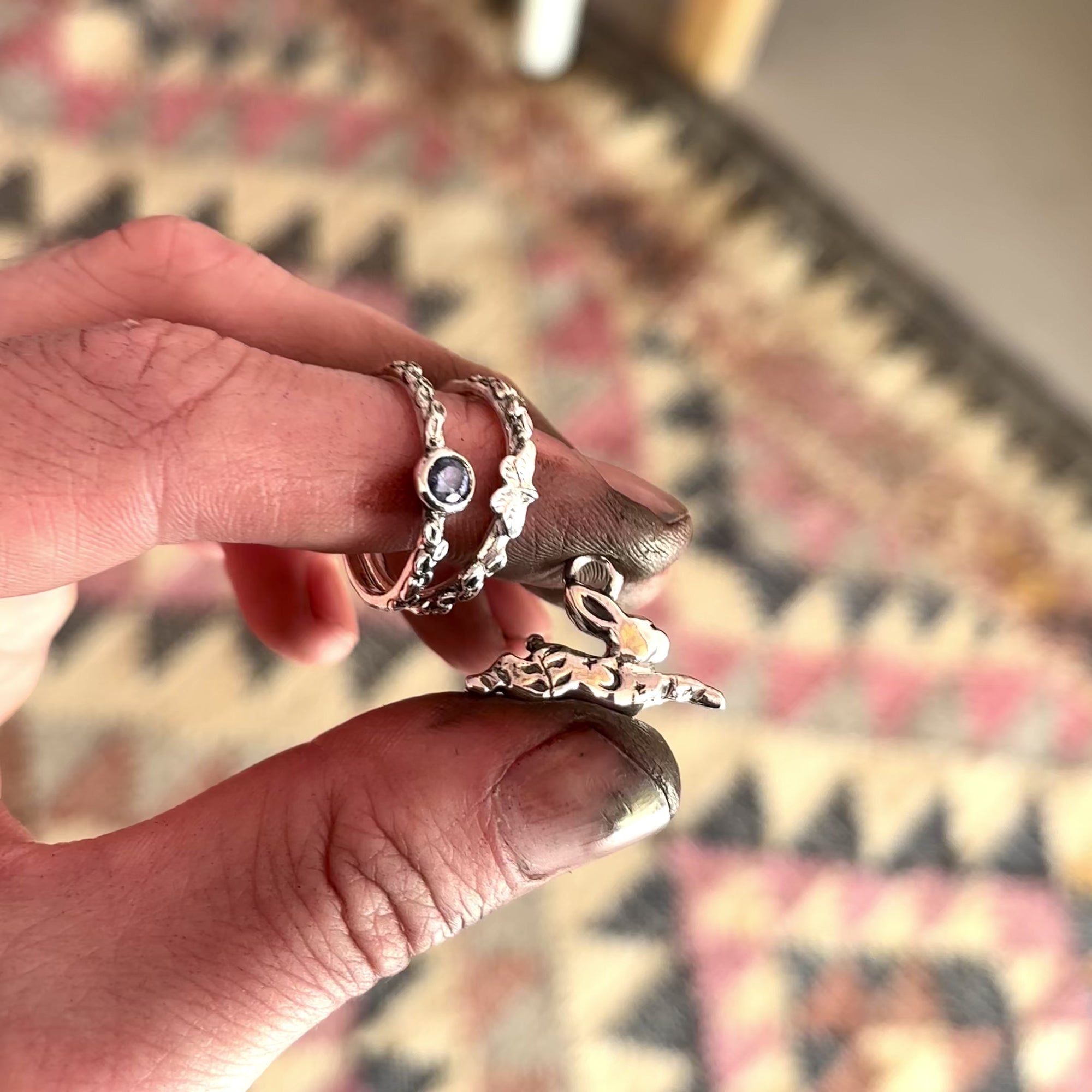 A hand holding a rabbit pendant and two rings that have just been polished. The hands are dirty and you can see a rug in the background. 