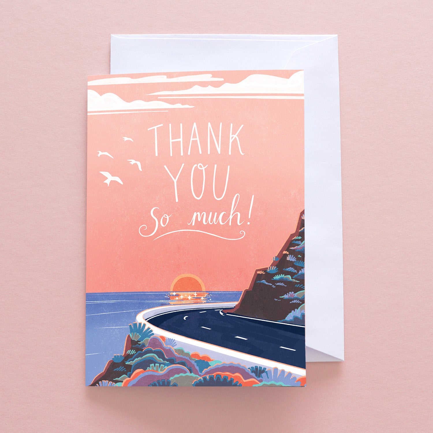 The Papio Press Thank You So Much Coastal Road Greetings Card features Thank you so much! on a pink sunset scene with a winding coastal road, colorful plants, and birds. Includes envelope. Printed on recycled stock.