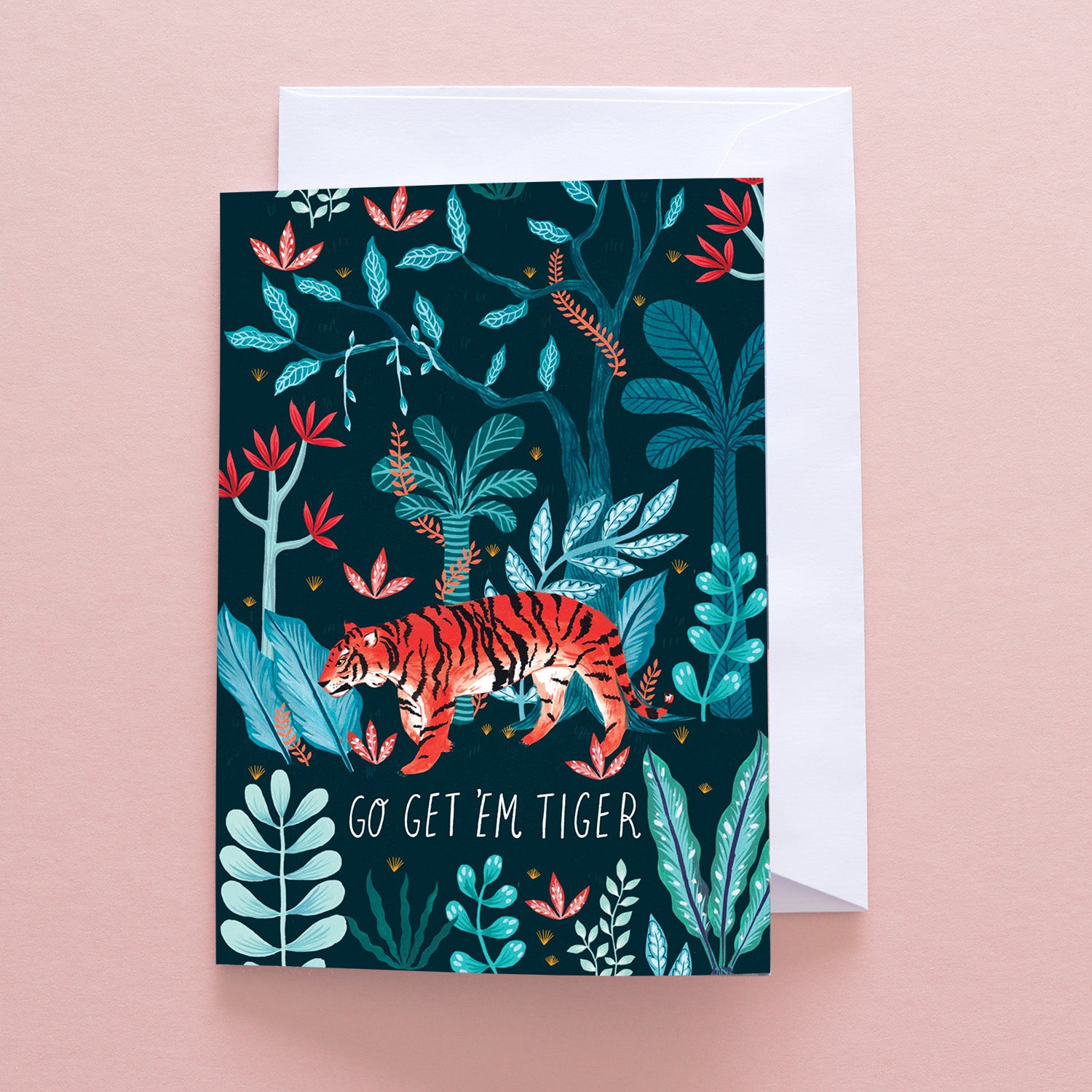 Papio Press Go Get Em Tiger Greetings Card features an orange tiger in vibrant jungle plants on a dark background. Printed on recycled stock, it reads GO GET EM TIGER and includes an envelope displayed beneath on a pink surface.