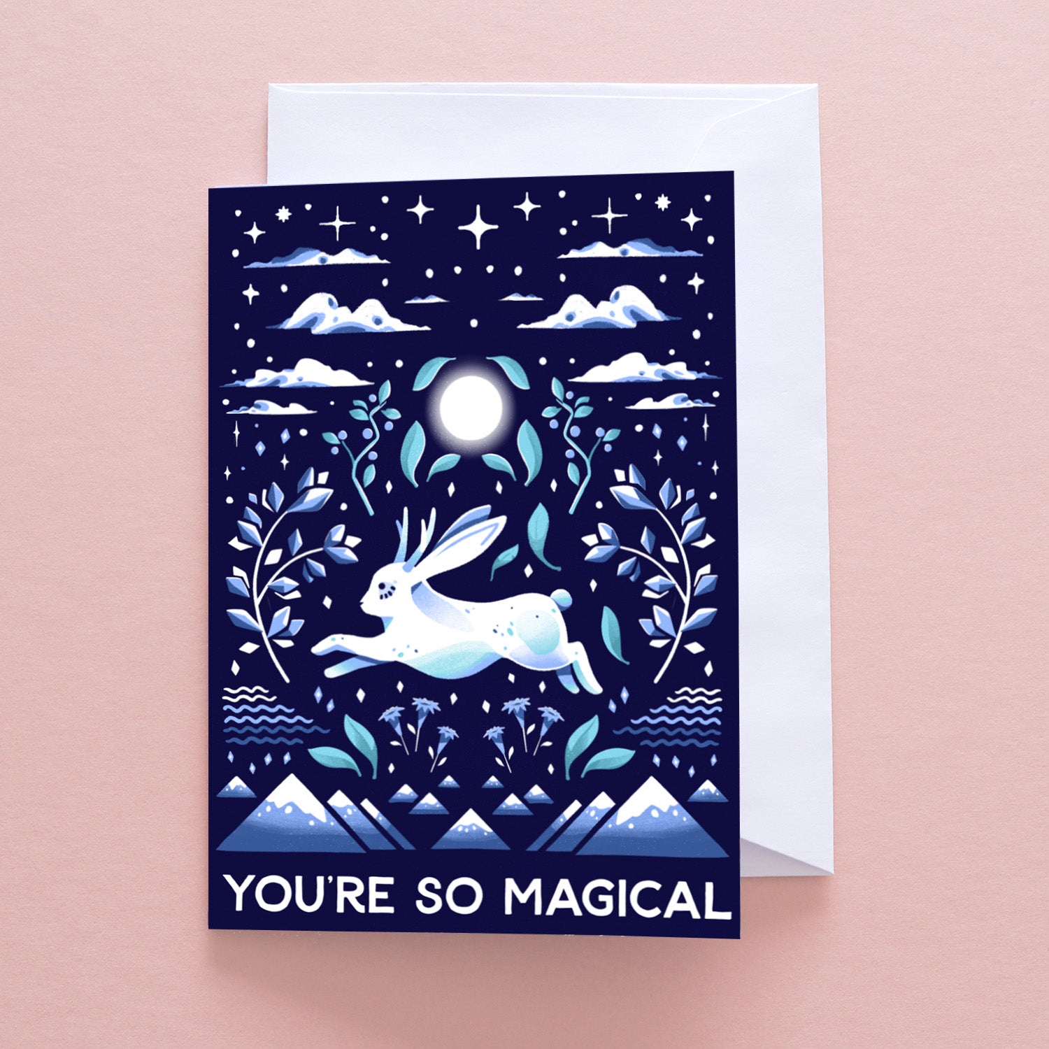 The Papio Press Youre Magical Jackalope Greetings Card features a white jackalope under a full moon with stars, clouds, and plants. Printed in blue and white on recycled stock, it reads YOURE SO MAGICAL at the bottom.