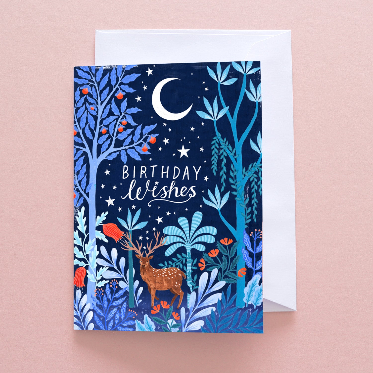 The Papio Press Birthday Wishes Stag Greetings Card features a deer in a colorful forest under a crescent moon and stars. Printed on recycled stock, it includes a white envelope and is presented on a pale pink background.