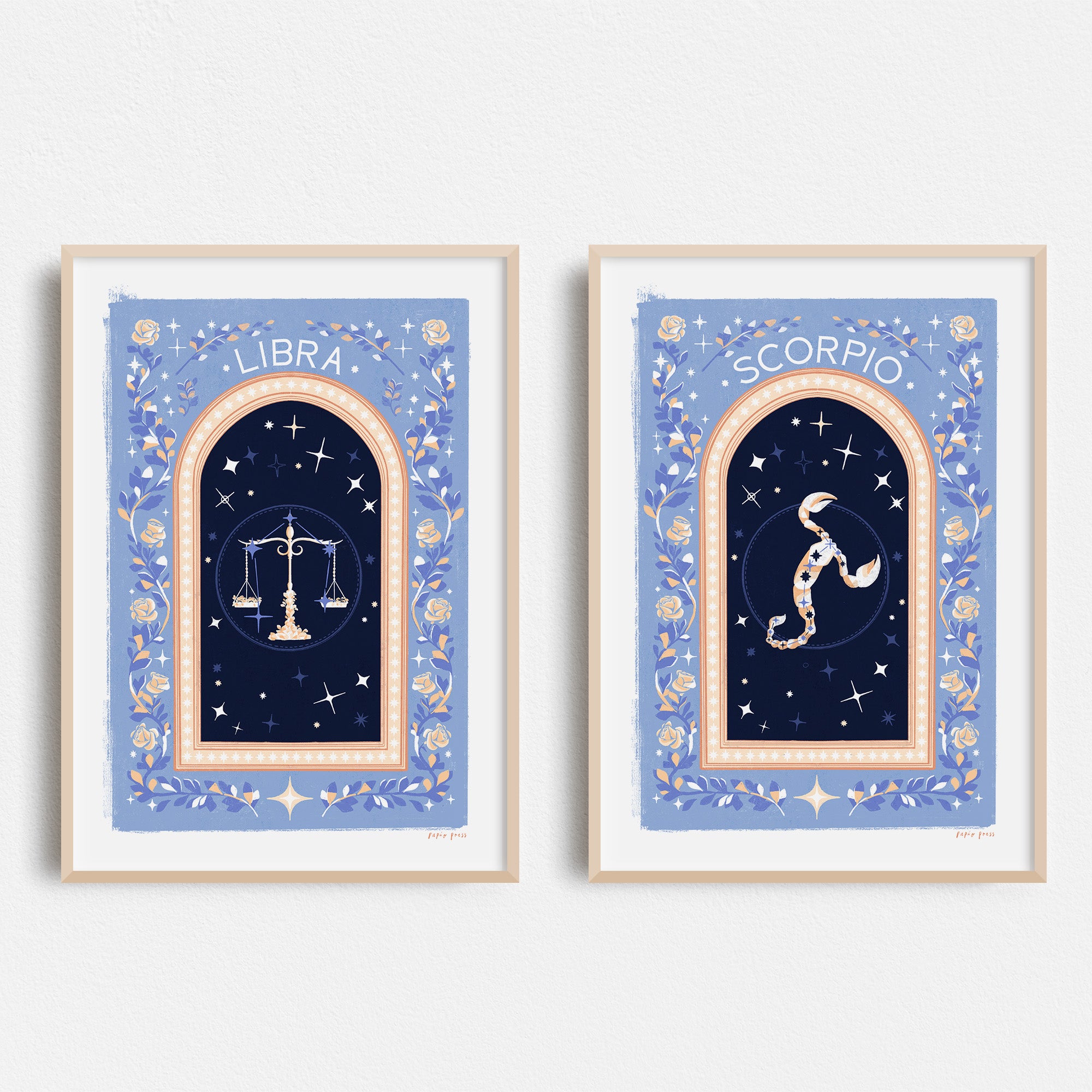 Two framed Choose Your Own Constellation Print // Star Signs by Papio Press hang on a white wall—Libra with scales and Scorpio with a scorpion—both on blue backgrounds, featuring star motifs and decorative borders, printed on archival satin paper.