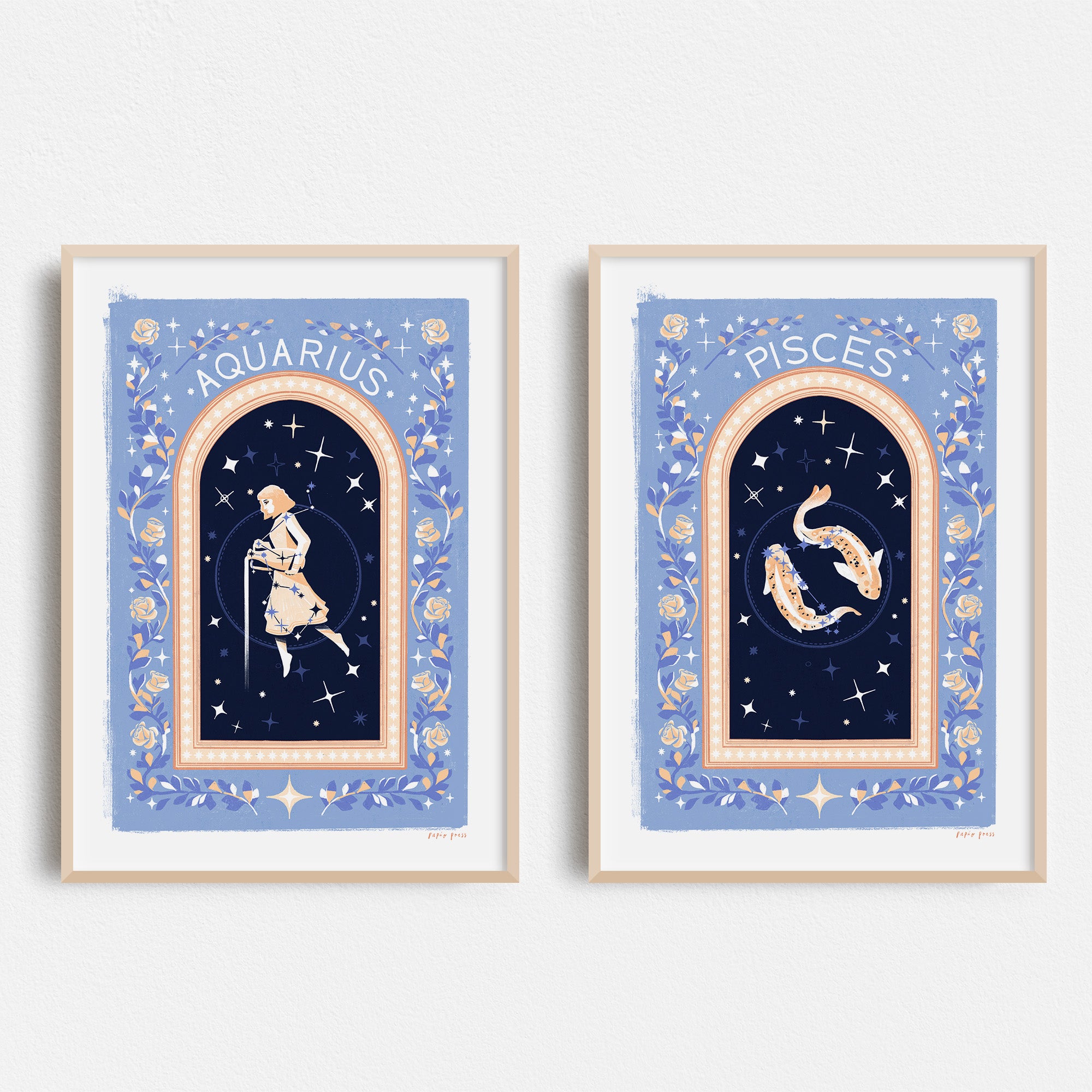 Two Choose your own Constellation Print // Star Signs art prints by Papio Press hang on a white wall: Aquarius pouring water and Pisces as two swimming fish, both on archival satin paper with blue starry backgrounds and floral borders.